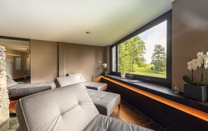 A modern spa room with a large window, a stone wall, and a seating area with cushioned chairs. - Lenkerhof Gourmet Spa Resort (Lenk)