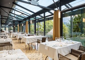 A restaurant with multiple tables set for dining, large windows, and a view of greenery. - Lenkerhof Gourmet Spa Resort (Lenk)