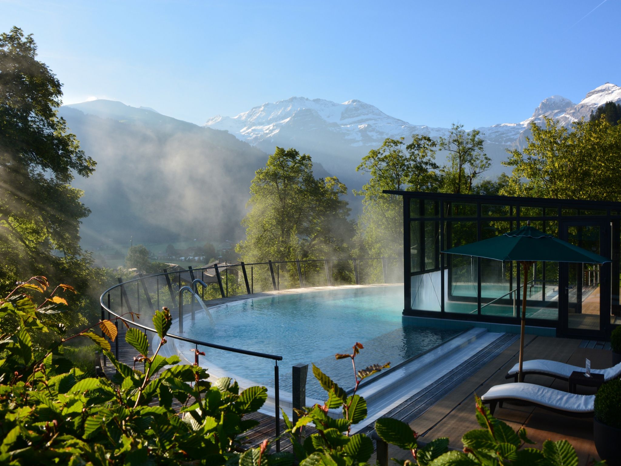 A spa pool with a glass enclosure, surrounded by lush greenery and a mountain backdrop.