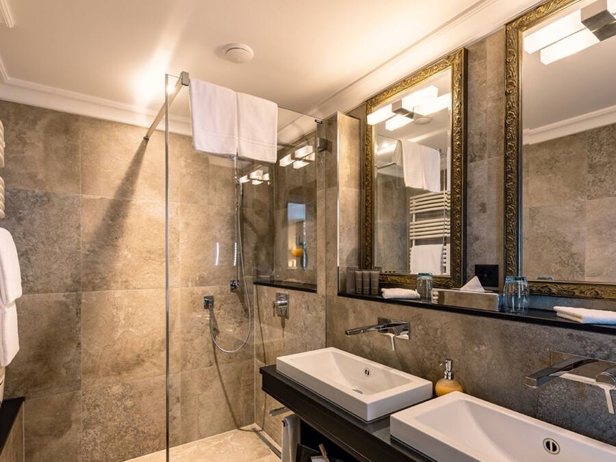 Un baño moderno con cabina de ducha de vidrio, dos lavabos y un espejo grande con marcos ornamentados.