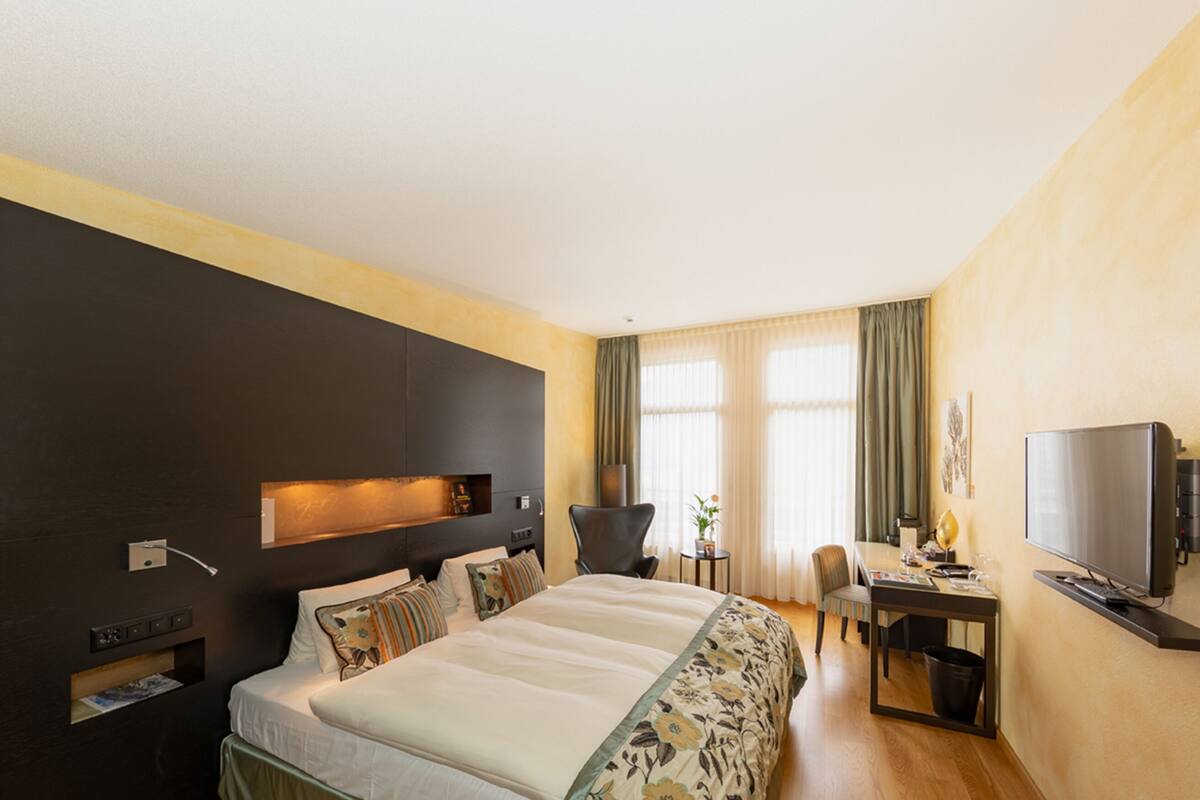 Una habitación de hotel con una cama grande, un escritorio con silla, un televisor y una mesita con una planta.