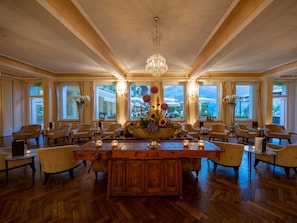 A spacious room with a large wooden table, multiple chairs, a chandelier, and large windows offering a view of the outdoors. - Lenkerhof Gourmet Spa Resort (Lenk)