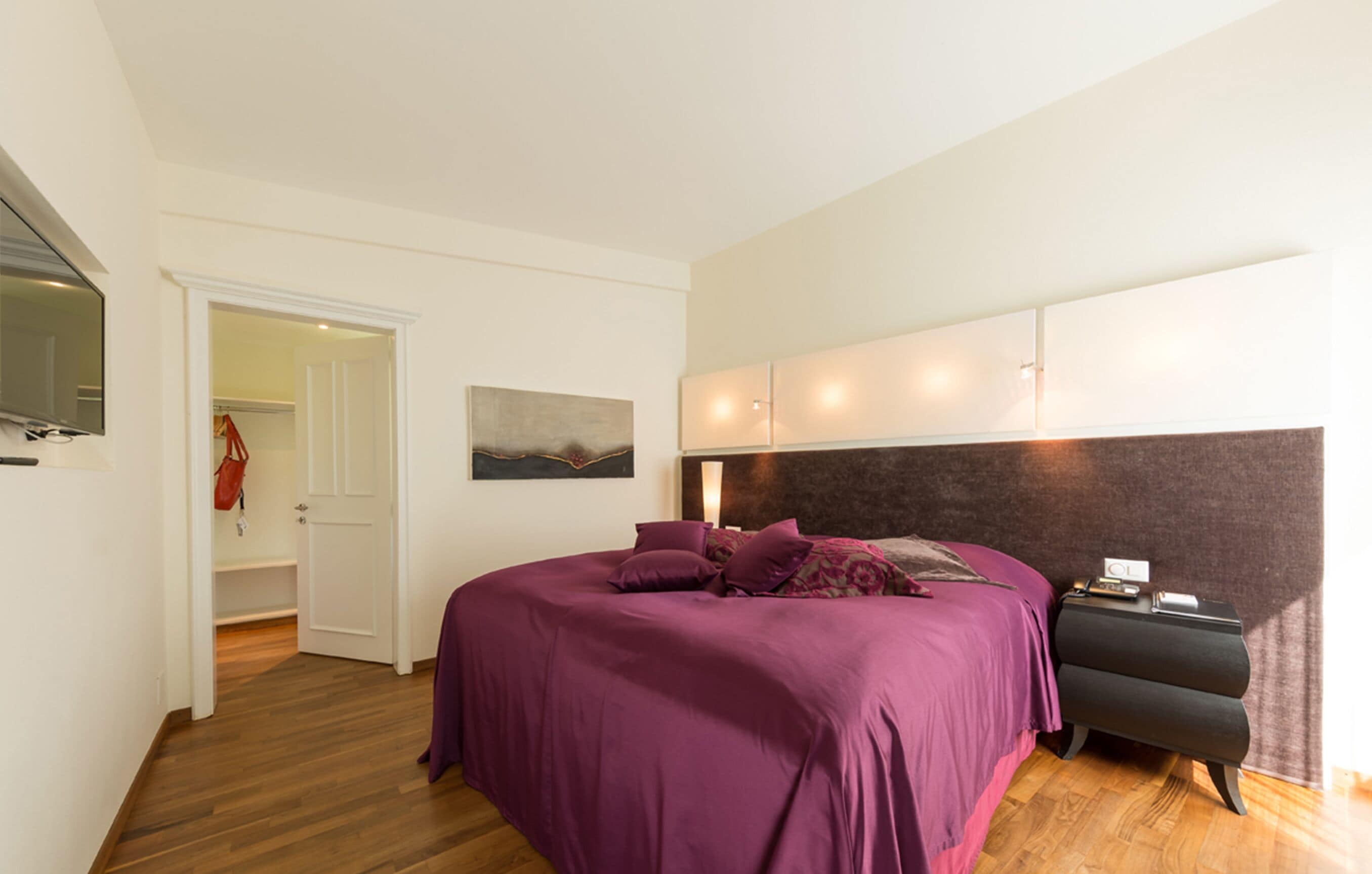 Un dormitorio con cama, mesita de noche y televisor montado en la pared.