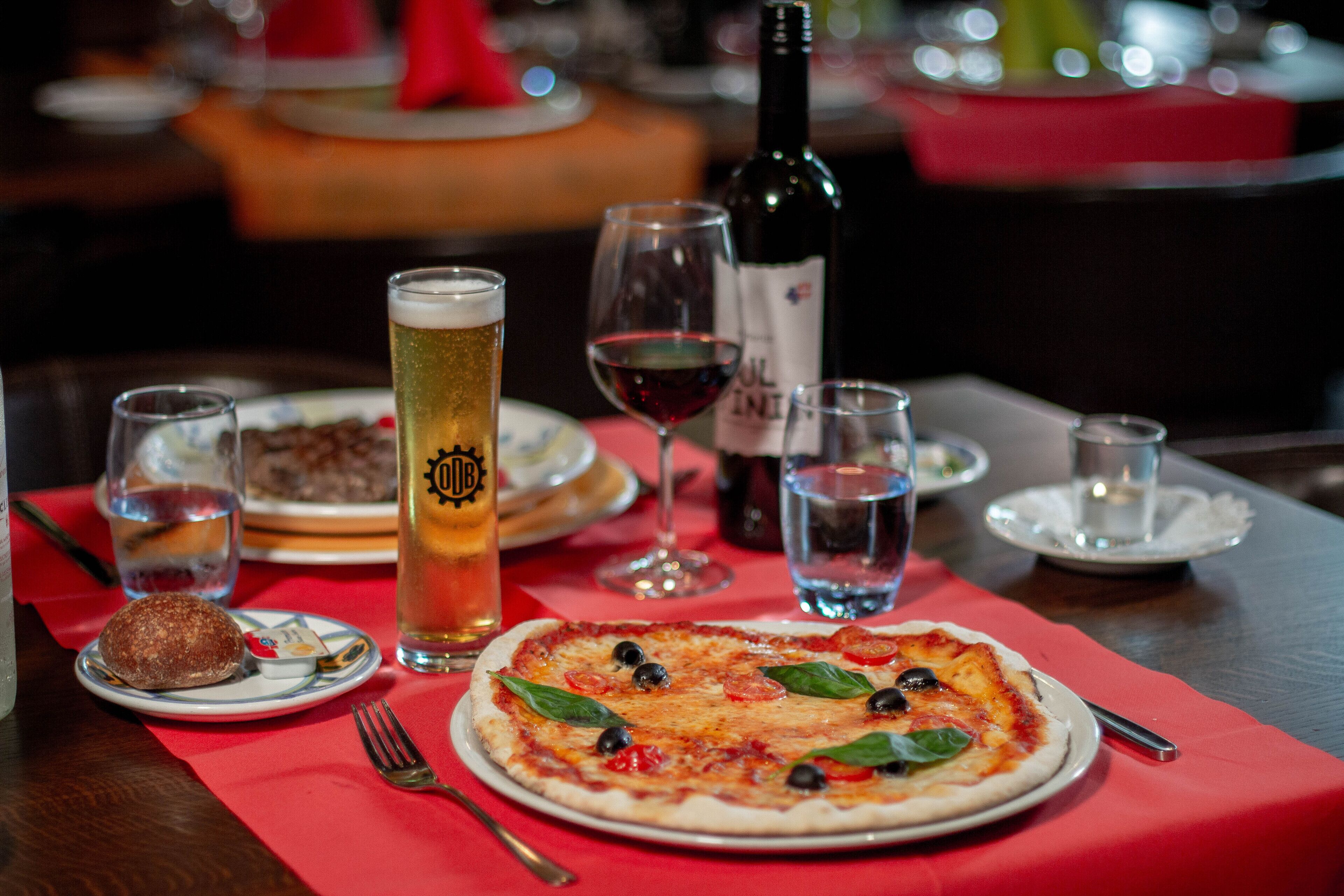 Une table à manger avec une pizza, une bouteille de vin et des verres de bière.