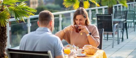 A couple dining at an outdoor table with a yellow tablecloth, surrounded by chairs and potted plants.