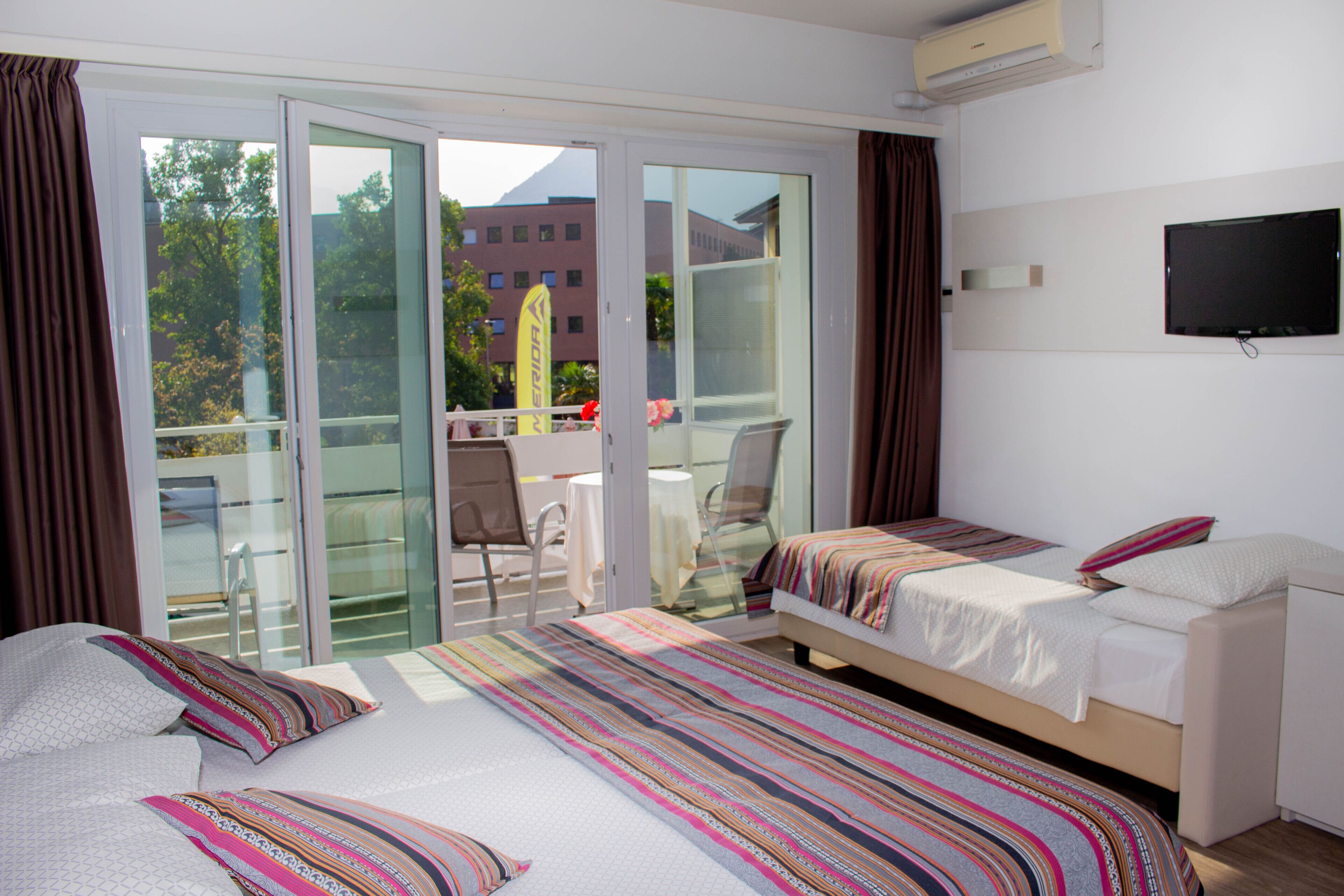 A hotel room with two beds, a TV, and a balcony with a table and chairs.