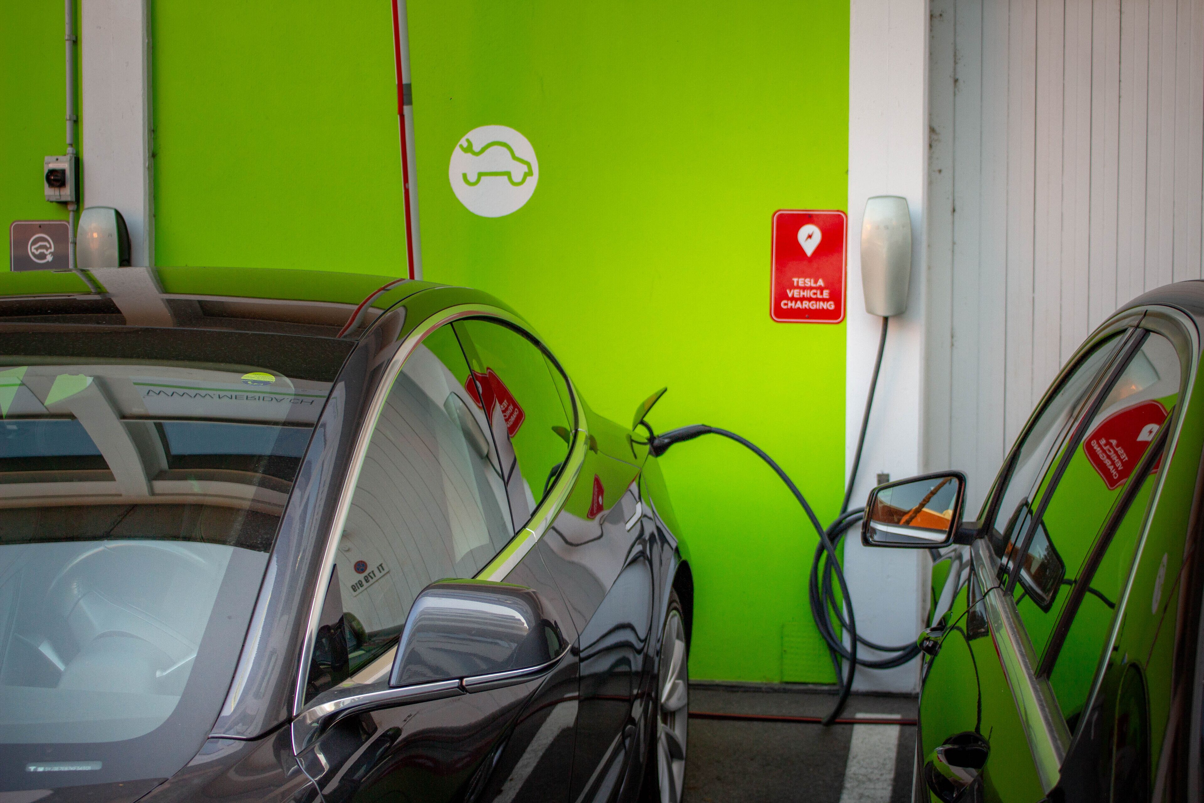A Tesla charging station with a green wall and a white door.