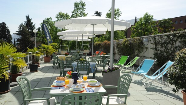 Un patio al aire libre con mesas, sillas, sombrillas y plantas en macetas.