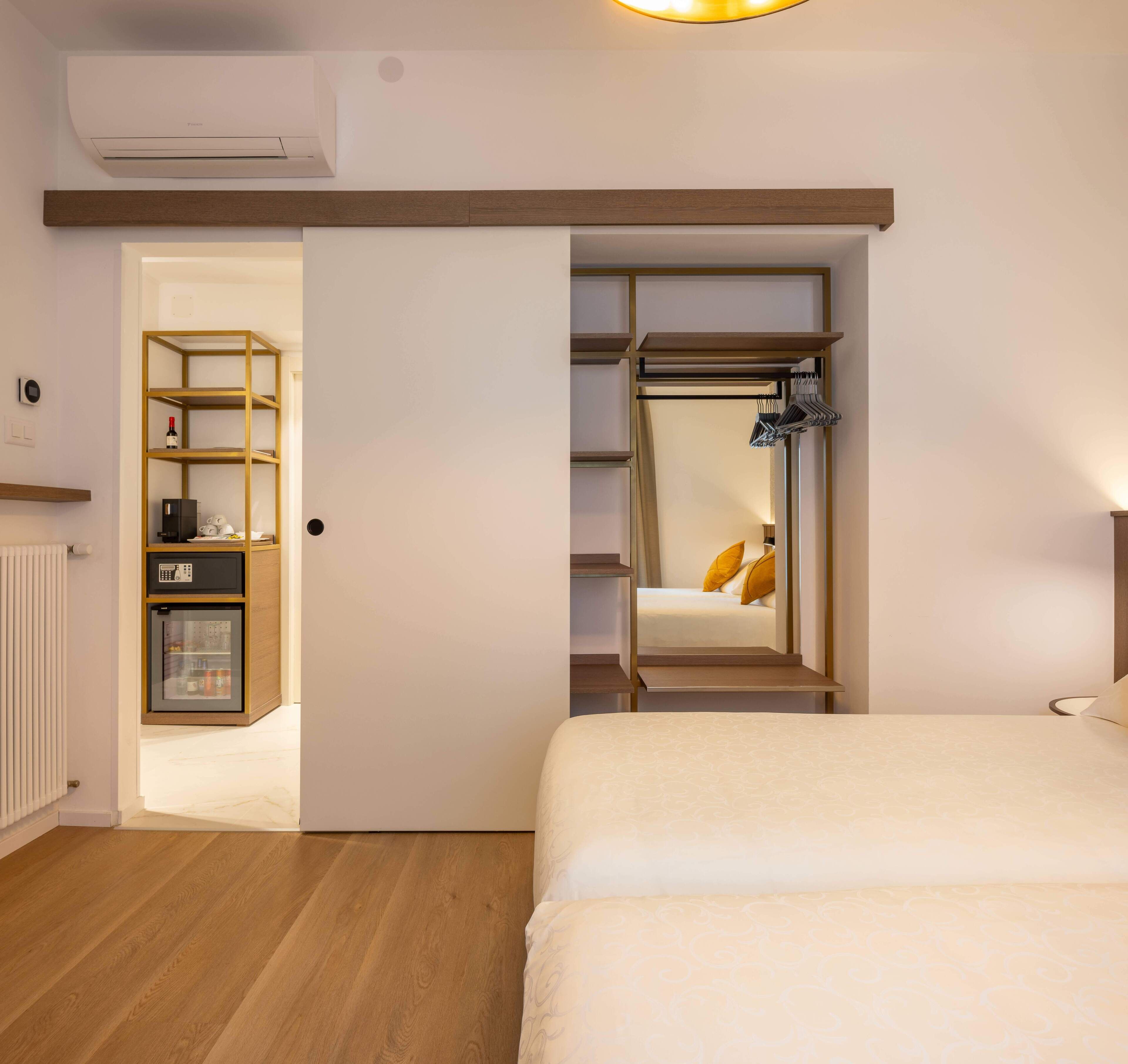 A bedroom with a bed, a wardrobe, a shelf unit, and a small refrigerator.