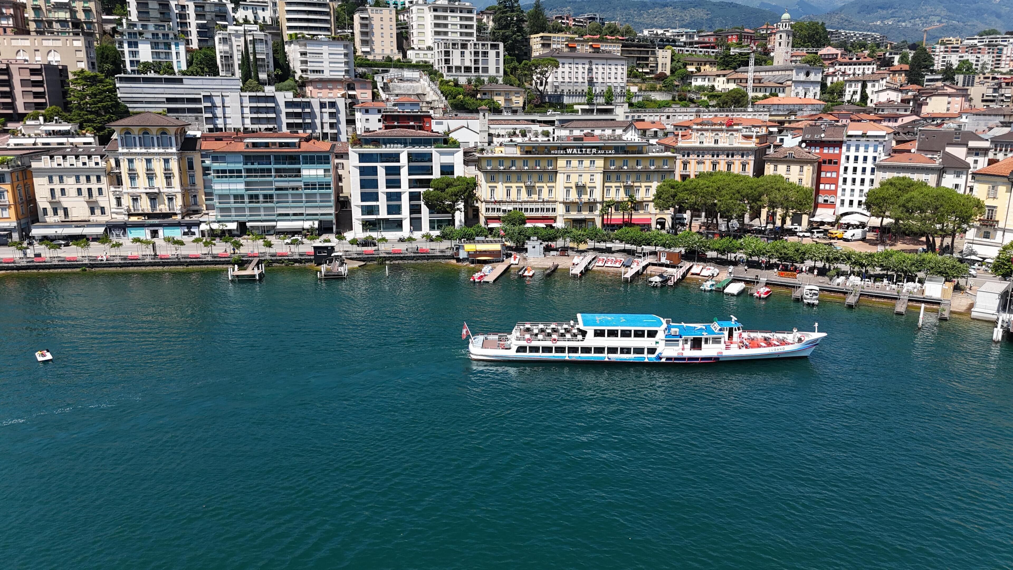 A waterfront cityscape with a large boat docked at a pier, surrounded by buildings and trees.
