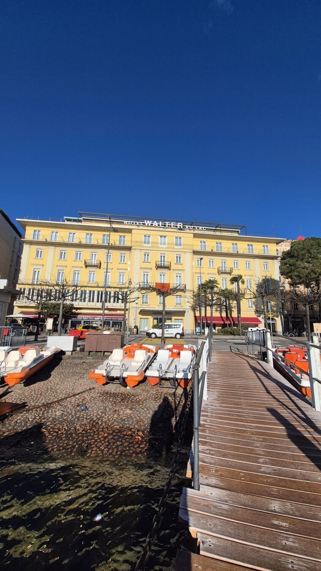 Un hotel de fachada amarilla, un muelle con barcos y un cielo azul despejado.