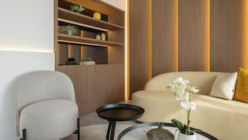 A modern living room with a sofa, armchair, and a round coffee table with a vase of flowers.