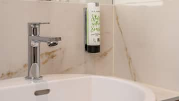 Un baño con lavamanos blanco, grifo cromado y dispensador de jabón de manos en la pared.