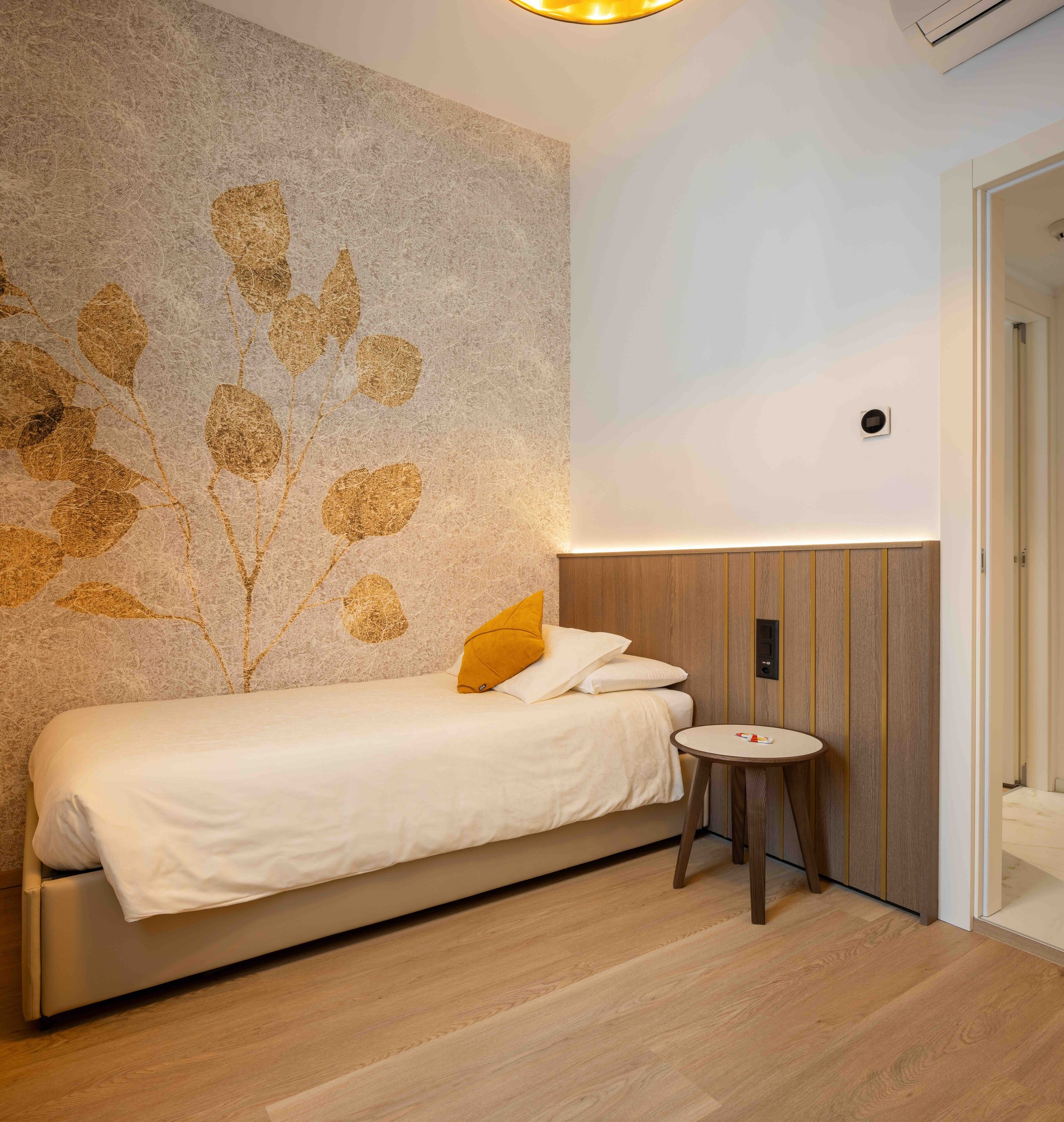 Ein modernes Schlafzimmer mit einem Bett, einem kleinen runden Tisch und einer Wand mit einem Blattmuster.