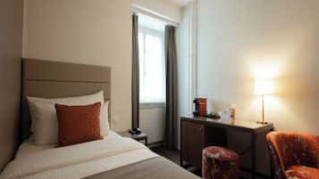 A hotel room with a bed, a desk, a chair, a lamp, and a window with curtains.