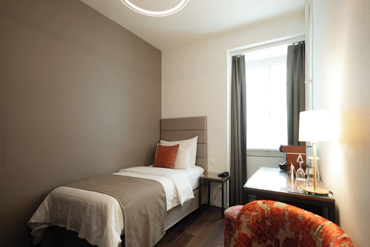 Quarto de hotel com cama, mesa de cabeceira, cadeira e janela com cortinas.