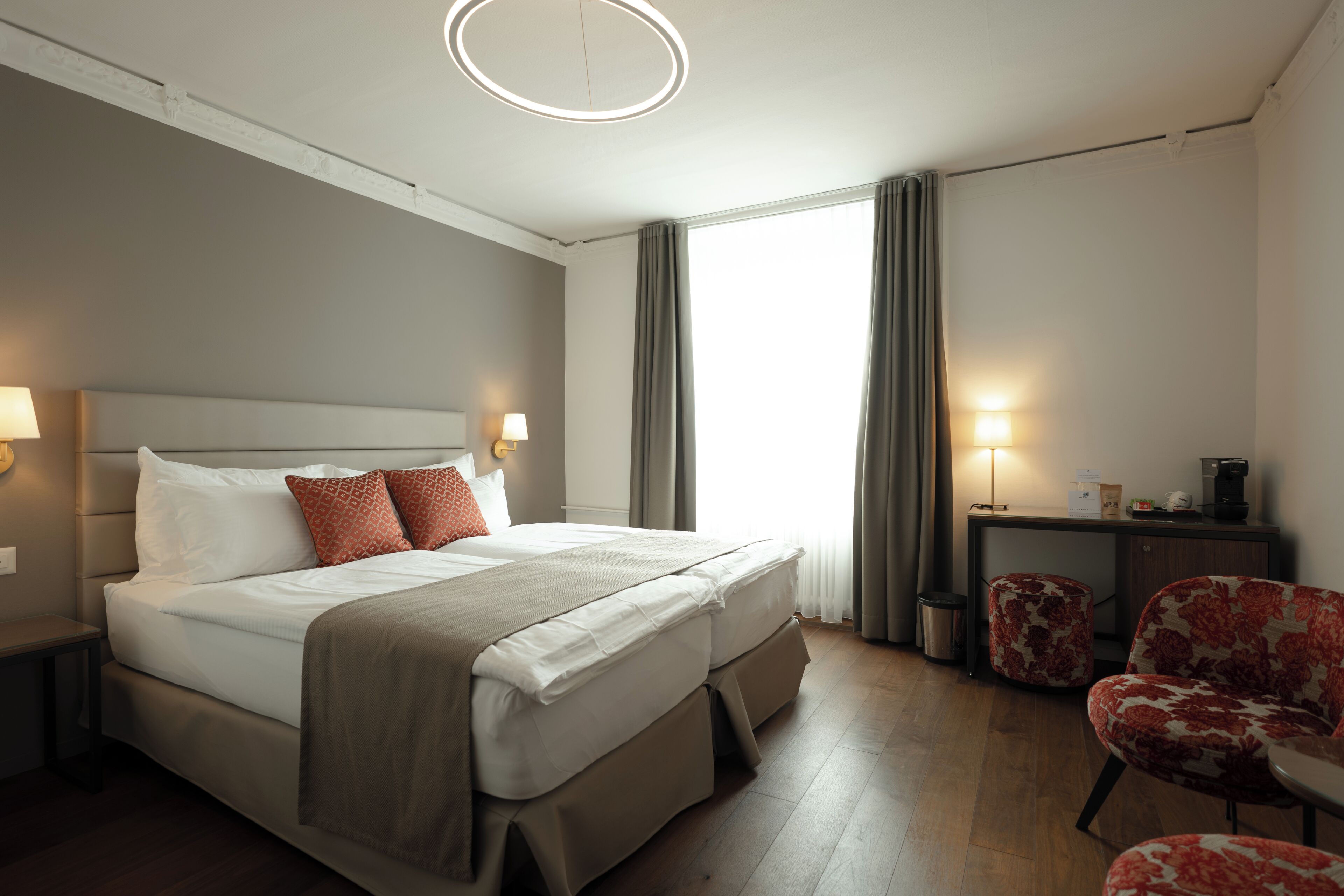 Una habitación de hotel con cama, lámparas de noche, un escritorio, una silla y un cesto de basura.