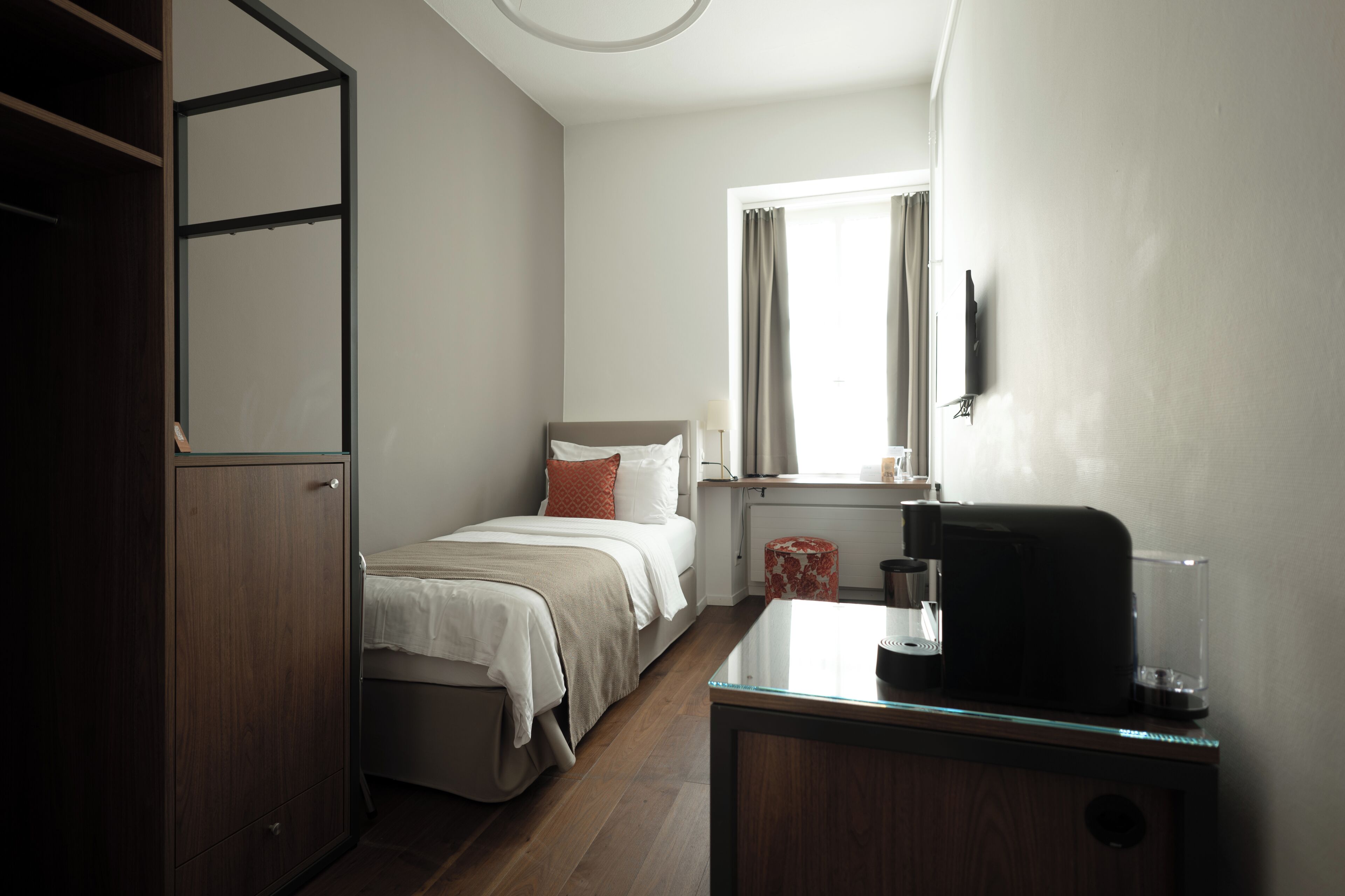 Un dormitorio con cama, escritorio, cafetera y ventana con cortinas.