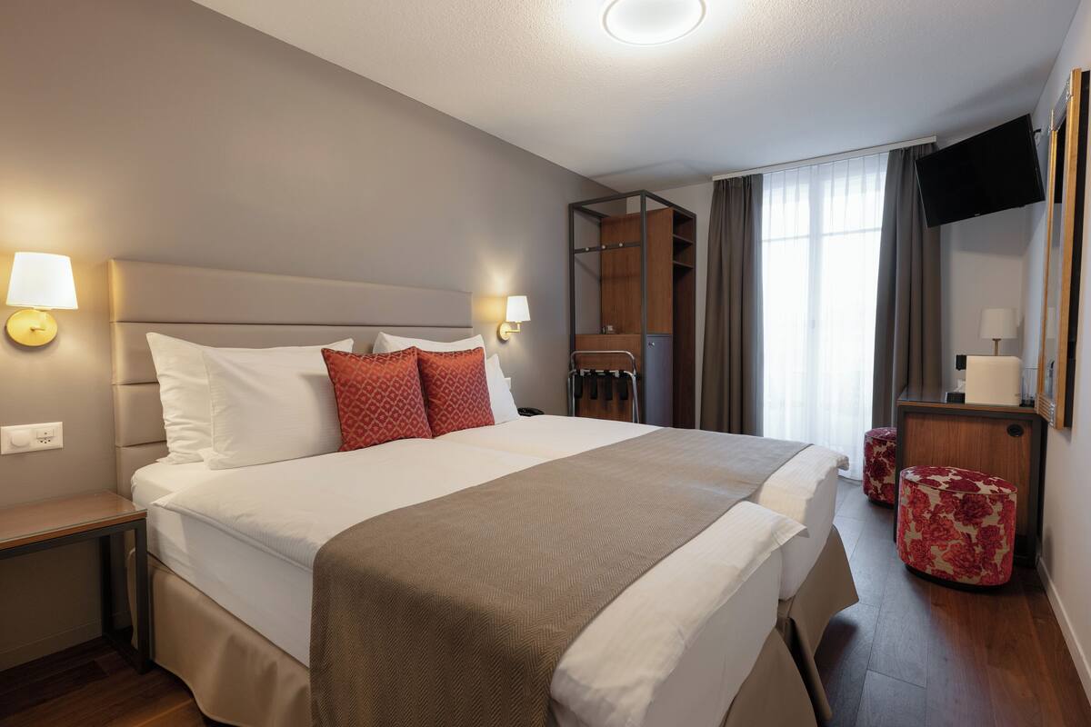 Quarto de hotel com uma cama grande, duas mesas de cabeceira, um guarda-roupa, uma TV e um espelho.