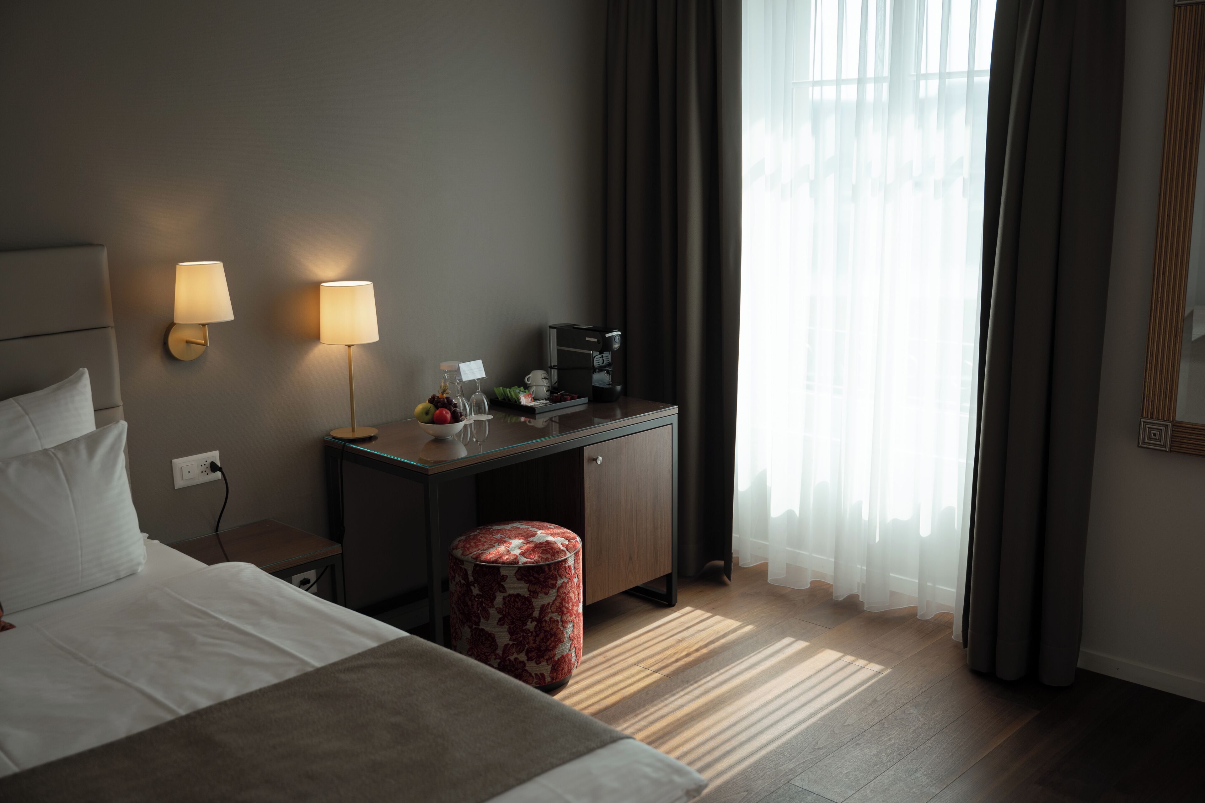 Une chambre d’hôtel comprenant un lit, des lampes de chevet, un bureau avec une machine à café et un pouf rond.