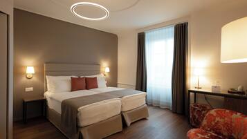 A hotel room with a bed, bedside lamps, a desk with a lamp, a chair, and a large window with curtains.