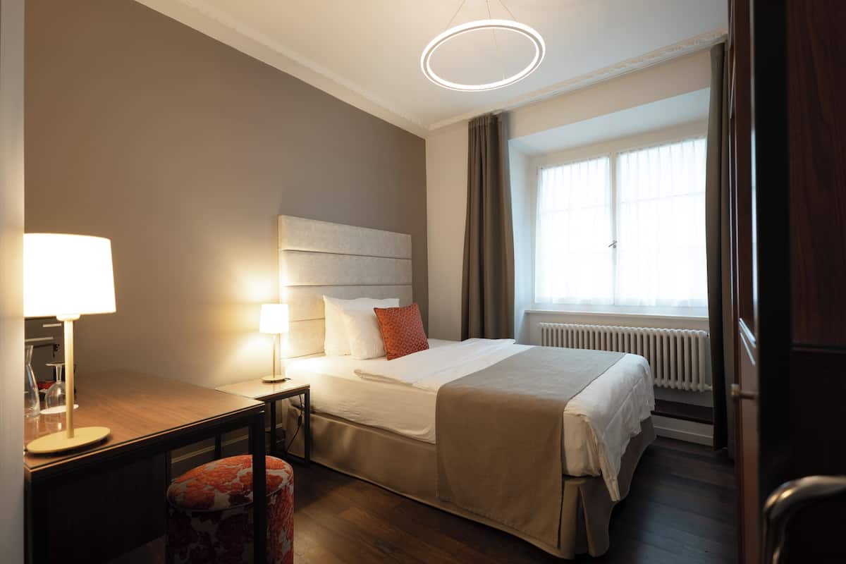 Quarto de hotel com cama, abajures, uma escrivaninha e uma cadeira.