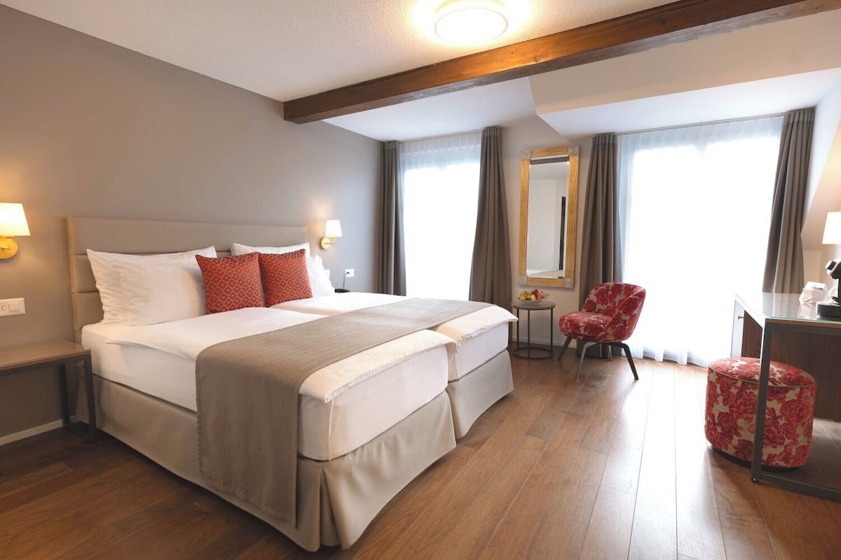Quarto de hotel com uma cama grande, uma escrivaninha, uma cadeira e um espelho.