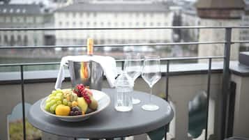 Ein Tisch mit Obstschale, einer Champagnerflasche und zwei Gläsern auf einem Balkon mit Blick auf eine Stadtlandschaft.
