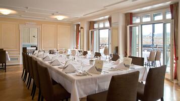 A dining room with a long table set for a meal, large windows with curtains, and a view of the cityscape.