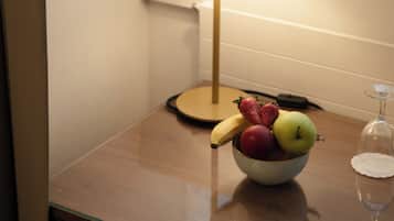 Una mesa con un bol de fruta, una lámpara y una copa de vino.