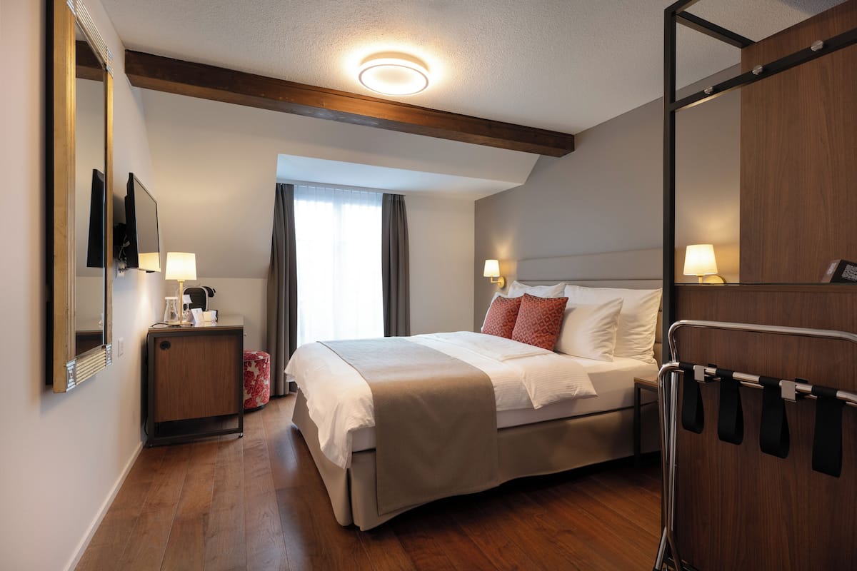 Quarto de hotel com cama, abajures, mesa de cabeceira, espelho e guarda-roupa.