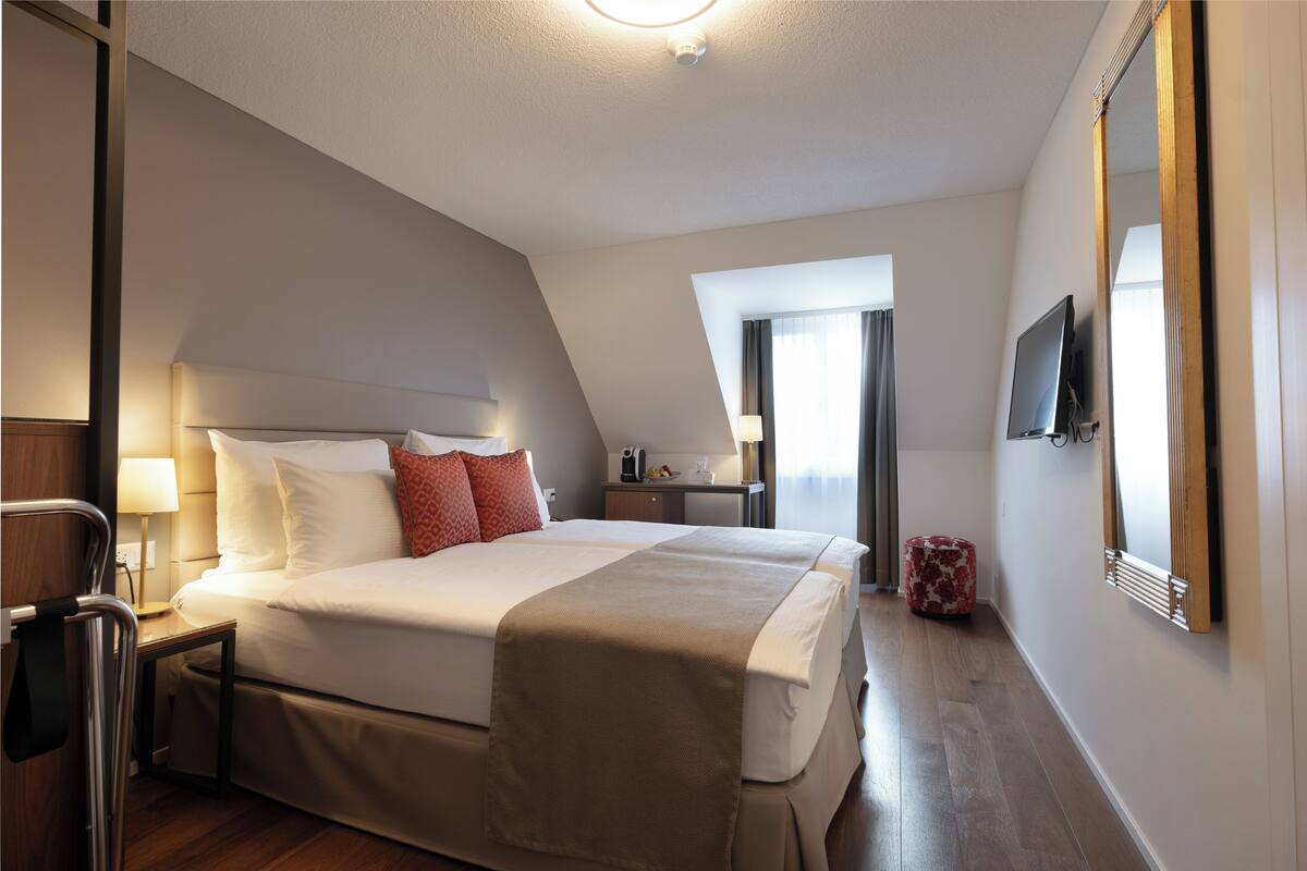 Quarto de hotel com uma cama grande, uma televisão, um espelho e uma mesa com abajur.