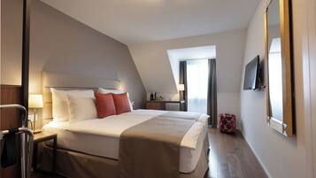 A hotel room with a large bed, a TV, a mirror, and a desk with a lamp.