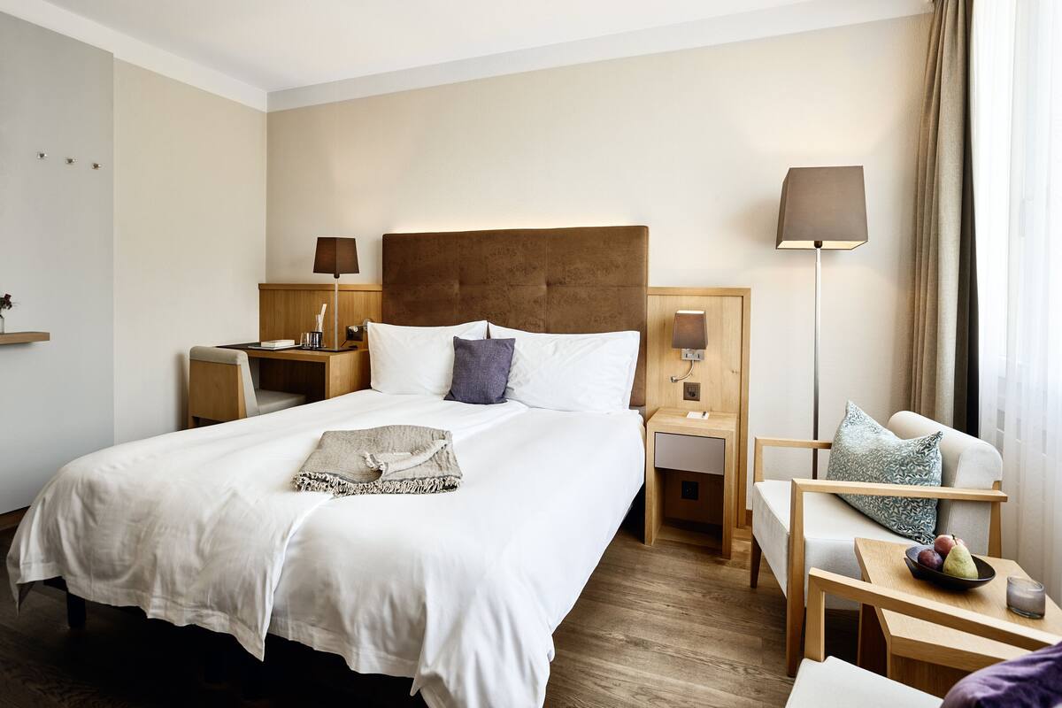 Ein Hotelzimmer mit einem großen Bett, einem Schreibtisch, einem Sessel und einem Nachttisch mit Lampe.