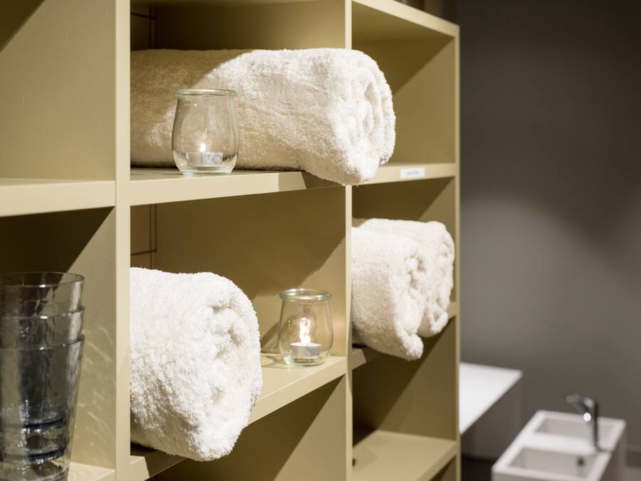 Une salle de bain avec des étagères où sont posées des serviettes blanches, une bougie en verre et un verre d’eau.