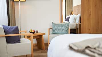 A hotel room with a bed, a desk, a chair, and a small table with a bowl of fruit.