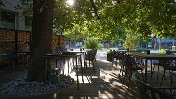An outdoor dining area with tables and chairs, surrounded by trees and a stone wall.