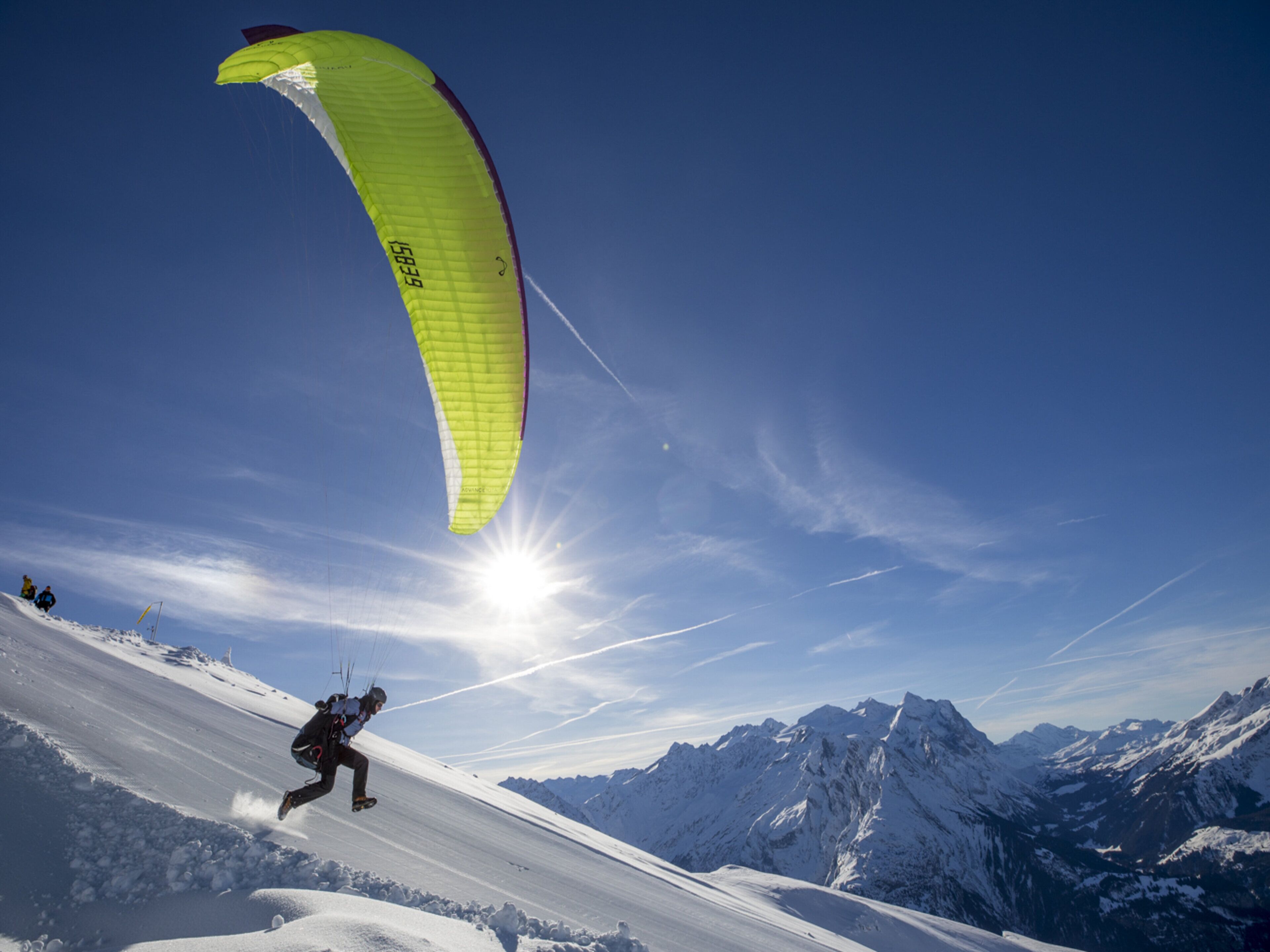 A person paragliding down a snowy slope with mountains in the background.