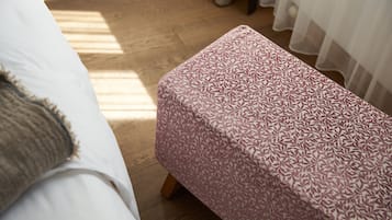 Un dormitorio con una cama, suelo de madera y un reposapiés estampado.