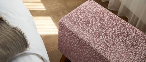 A bedroom with a bed, a wooden floor, and a patterned ottoman.