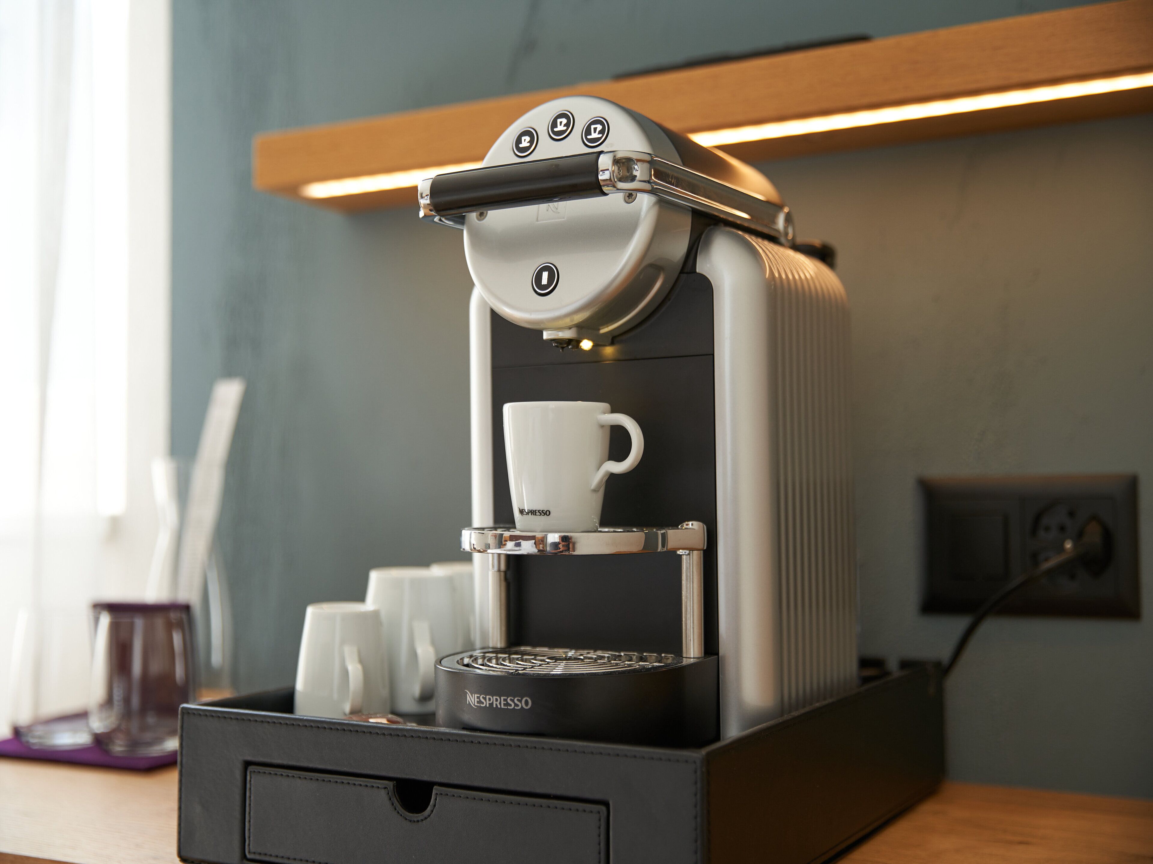 A Nespresso coffee machine with a cup holder and a drawer below it.
