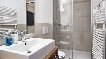 A modern bathroom with a large white sink, a glass shower enclosure, and a towel rack.