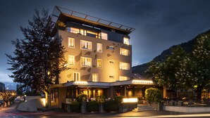 Un hotel de varios pisos con restaurante en la planta baja, con un diseño arquitectónico moderno que incluye grandes ventanales y tejado plano.