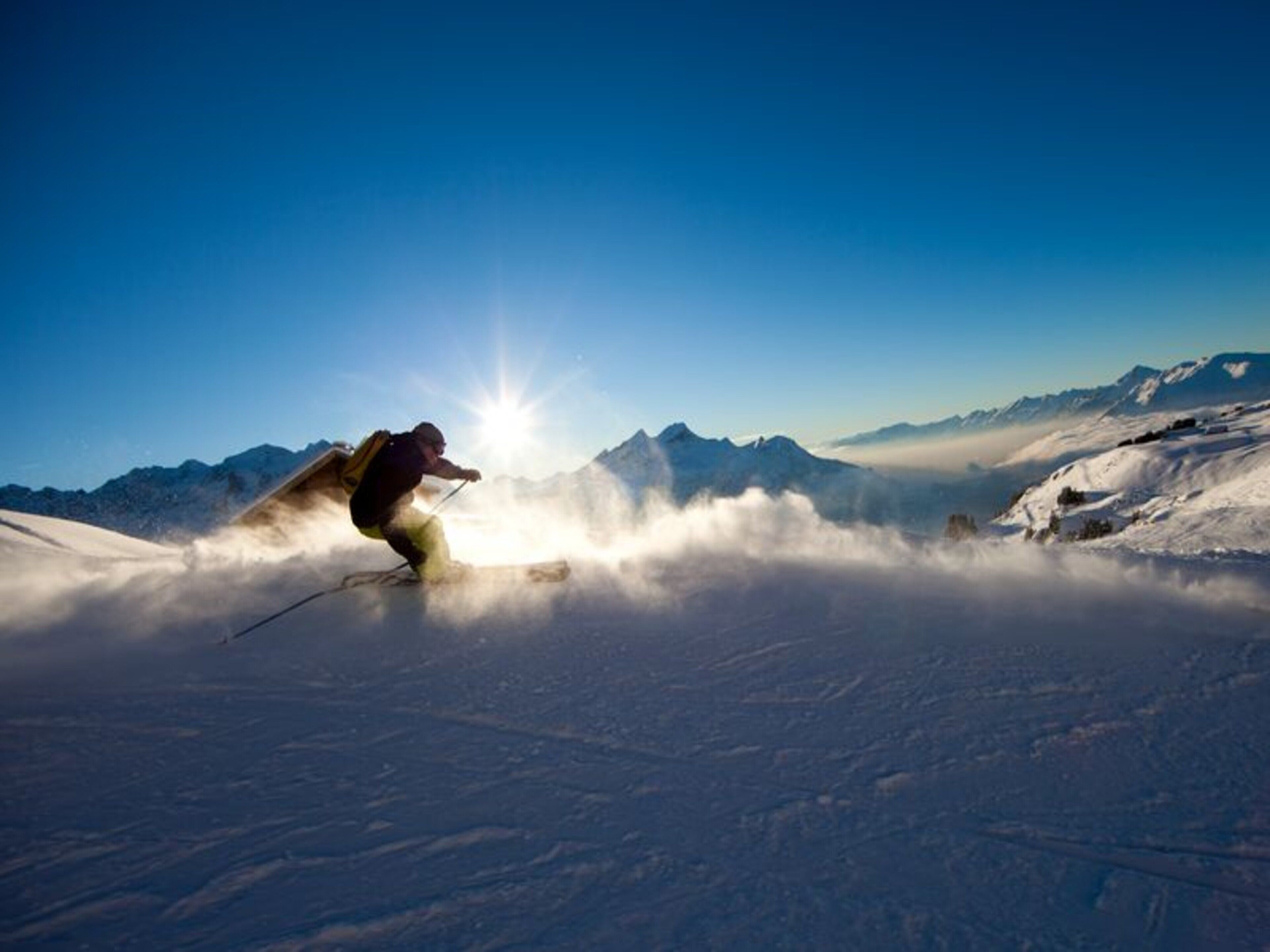 A skier on a snowy mountain with a clear sky and distant mountains.
