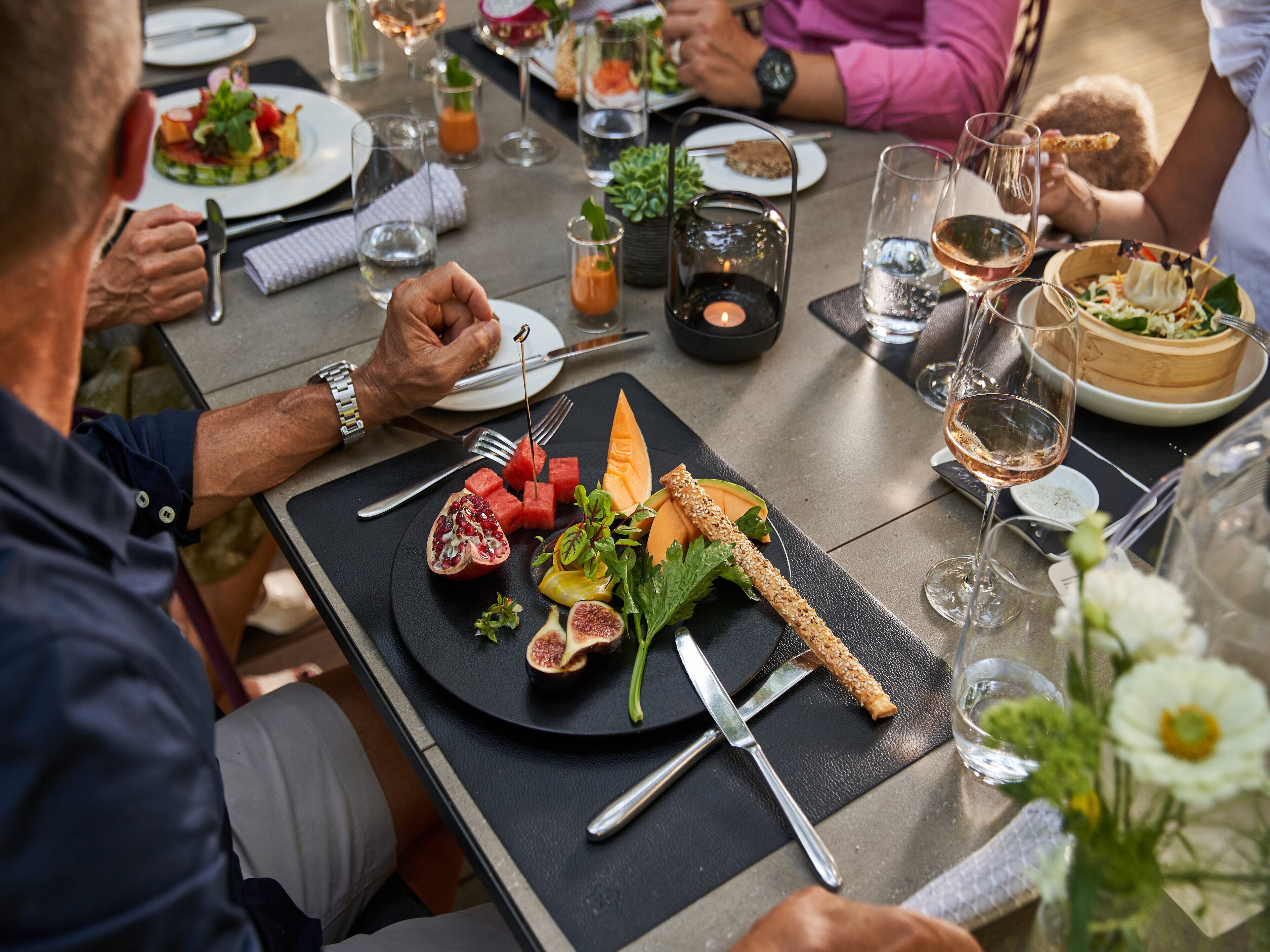 A dining table set with plates, cutlery, and glasses, surrounded by people engaged in conversation.