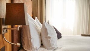 Una cama bien hecha con almohadas blancas y marrones, una mesita de noche con un libro y una lámpara.
