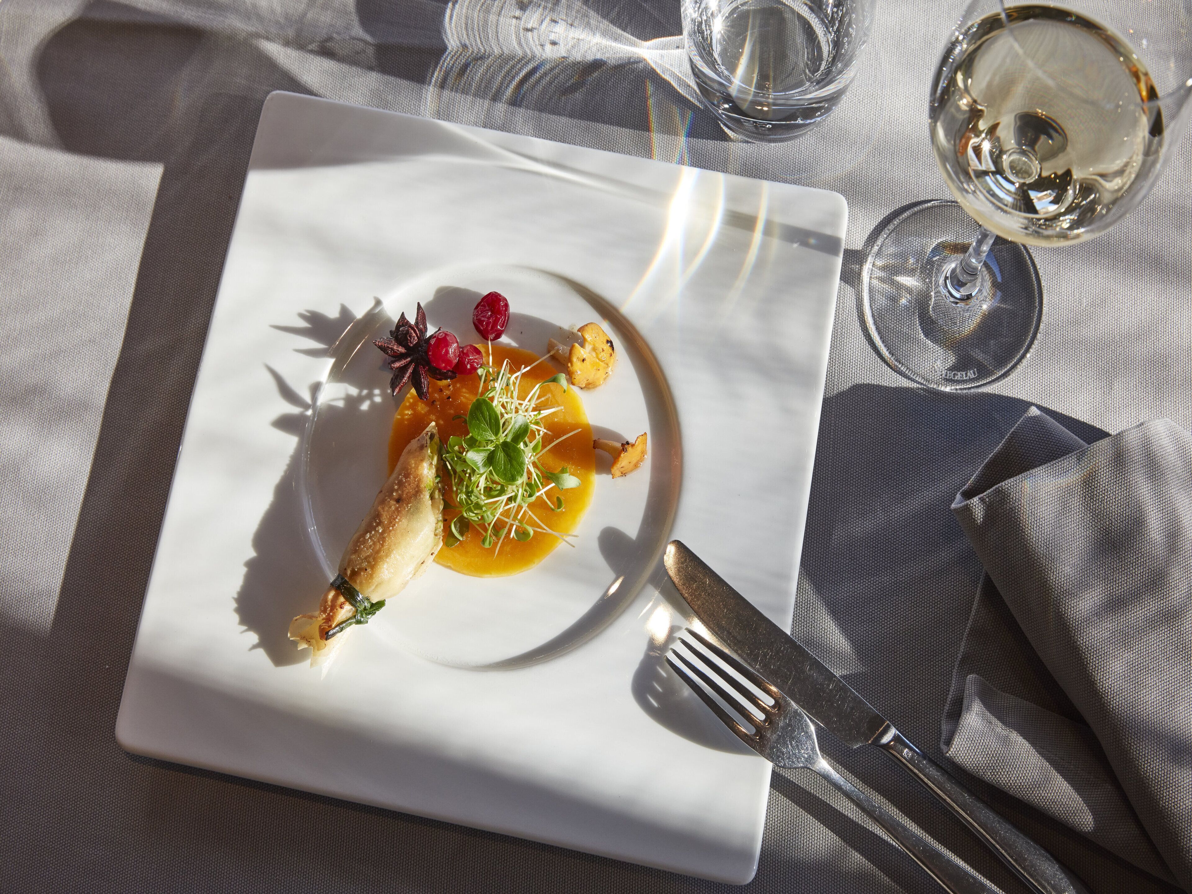A white plate with a dish, a fork, and a knife on a tablecloth.