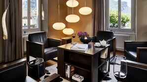 Habitación de hotel moderna con zona de comedor, ventanas amplias con vistas a la montaña y una estantería con libros y una vela.