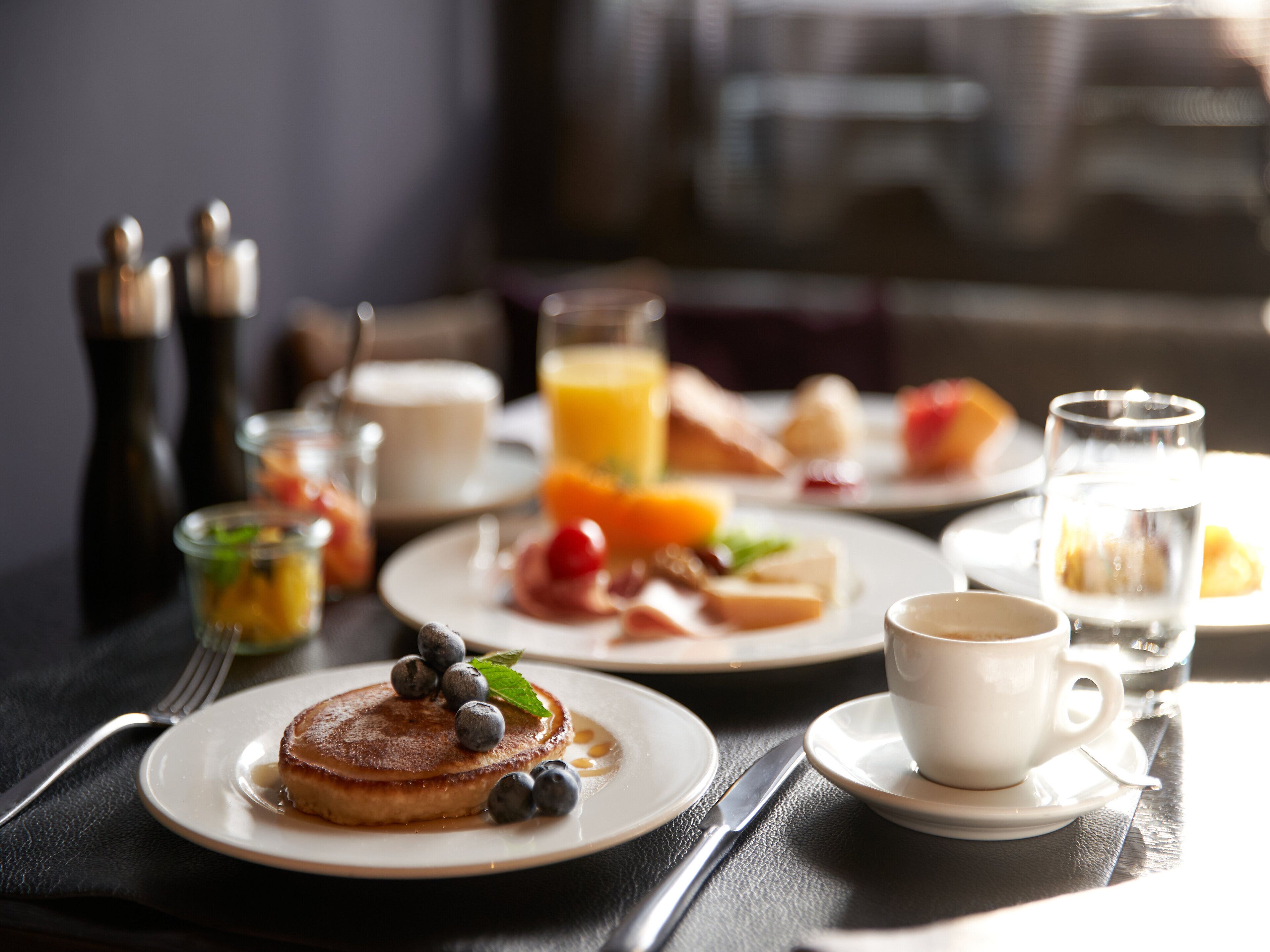 Une table dressée pour le petit-déjeuner, avec des crêpes, des fruits et du café.