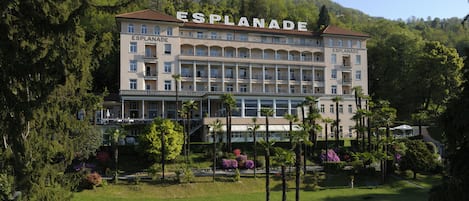 Un hotel grande con varios pisos y balcones, rodeado de abundante vegetación y un césped bien cuidado.